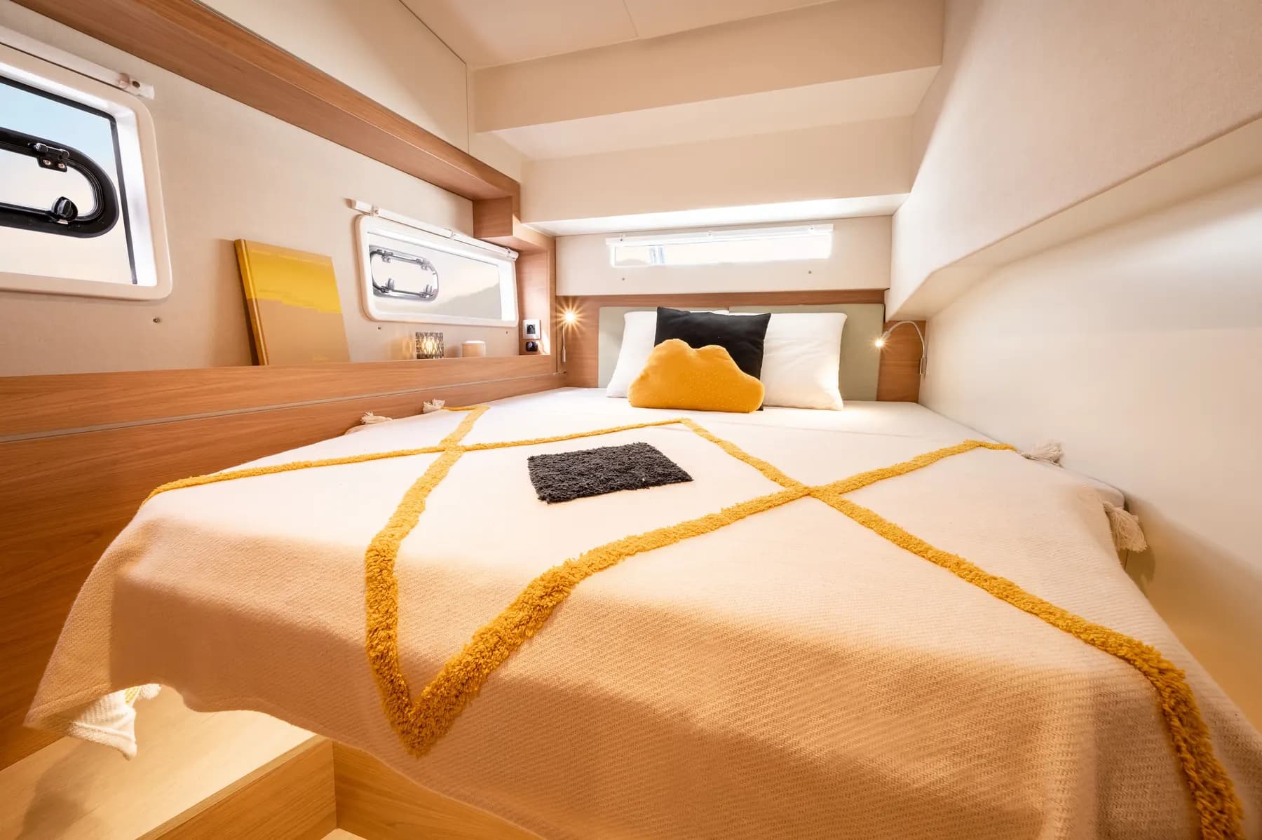 Double bed in a guest cabin of a Bali 4.2 catamaran, with a yellow-patterned cover and hull ports