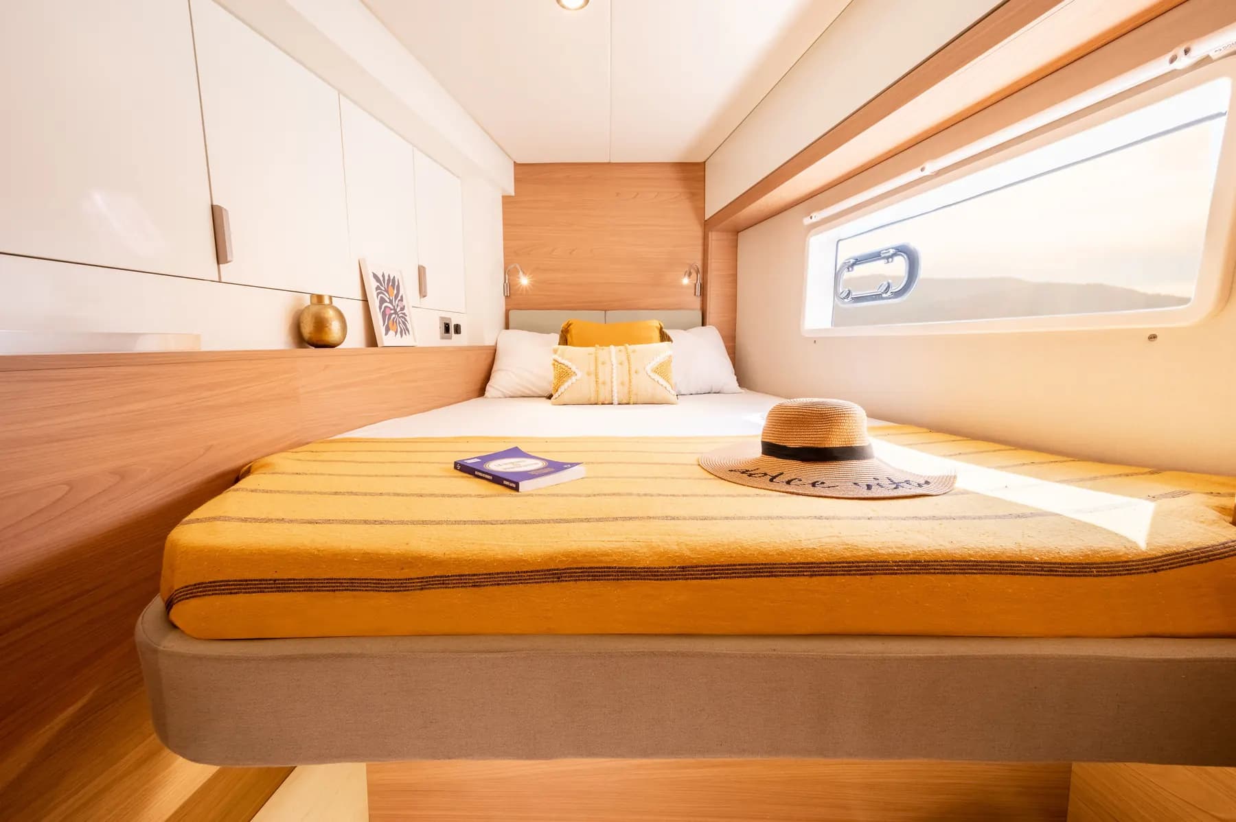 Double guest cabin of a Bali 4.2 catamaran, with a yellow throw on the bed and a window in the hull