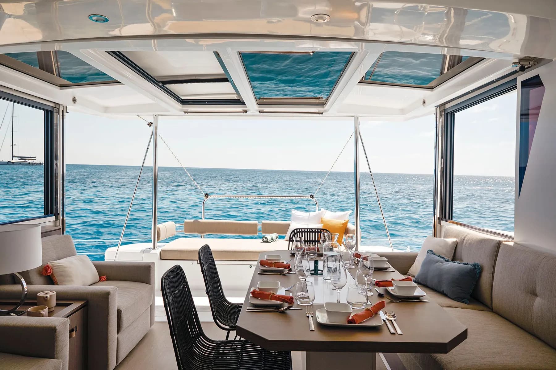 Saloon of a Bali 4.2 catamaran with the table laid and the tilting aft door open to the cockpit and the sea