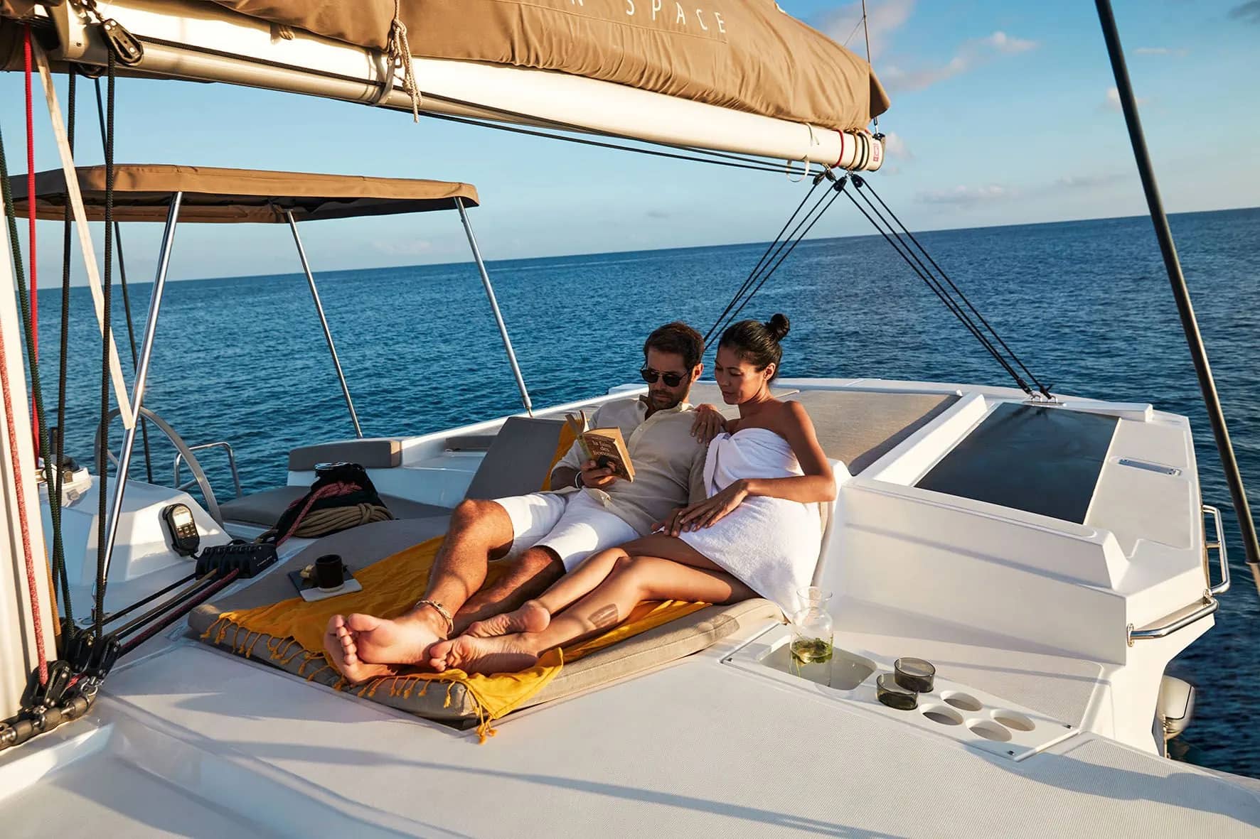 Two guests reading on the flybridge sunbed of a Bali 4.2 catamaran, under the bimini, with the sea behind