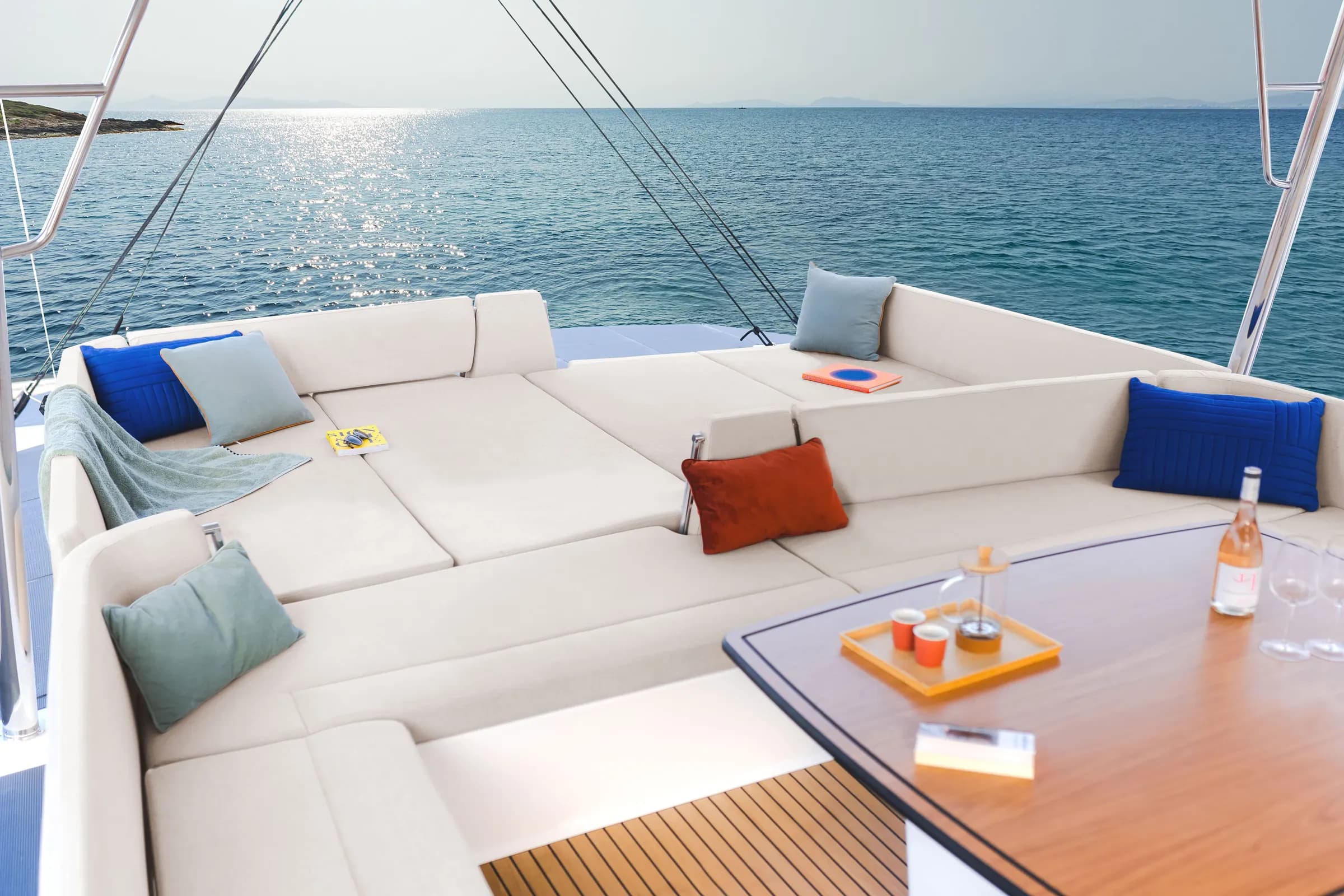 Forward cockpit lounge of a Bali 4.2 catamaran at sea, with white cushions, a teak table and the open horizon