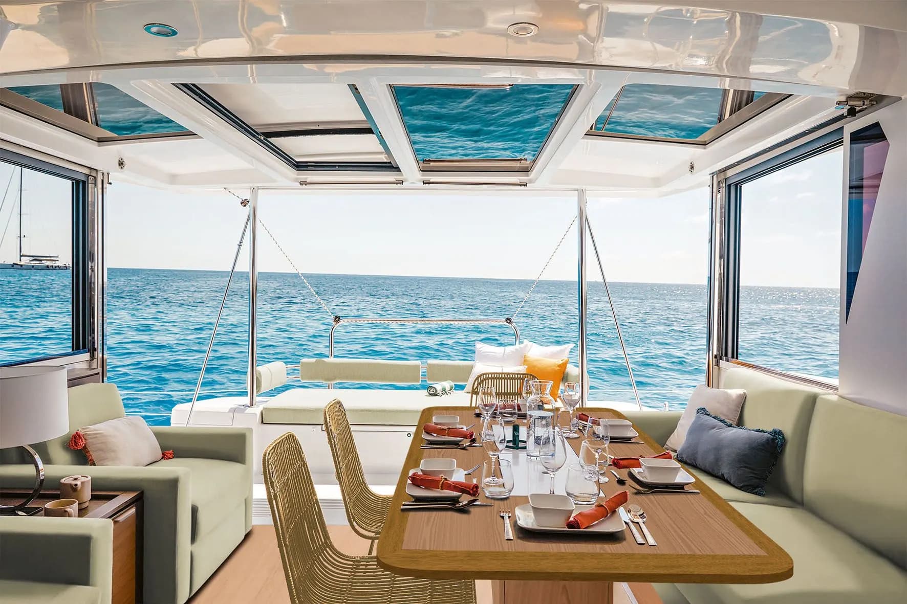Saloon of a Bali 4.2 catamaran: a laid dining table under the roof skylights, with the sea through open windows